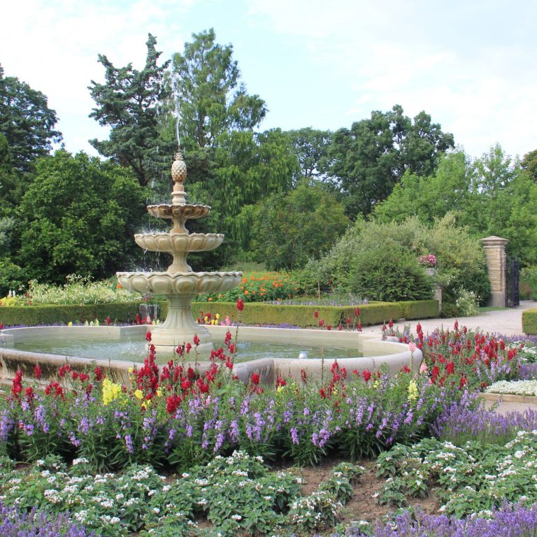 A large cement water fountain surrounded be a wildflower garden