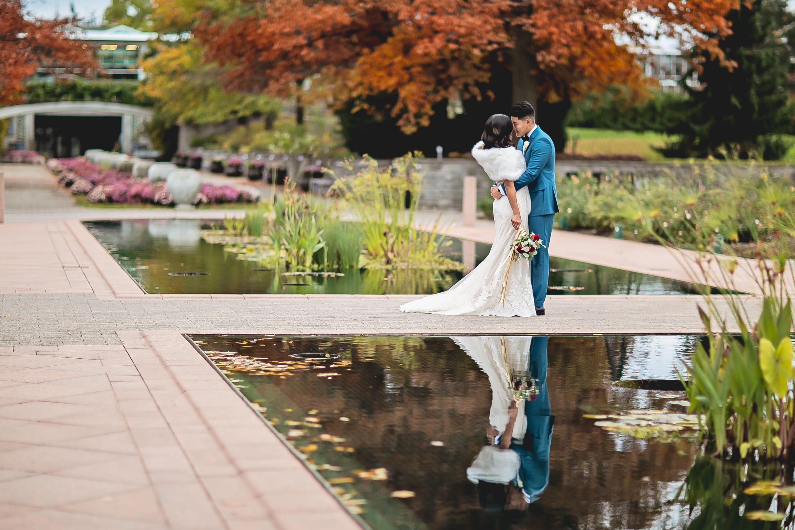 Bride and groom embracing at the edge of reflecting ponds, in fall