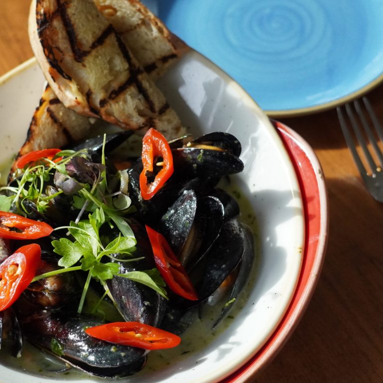 bowl of mussels in a white cream sauce, topped with sliced chilies