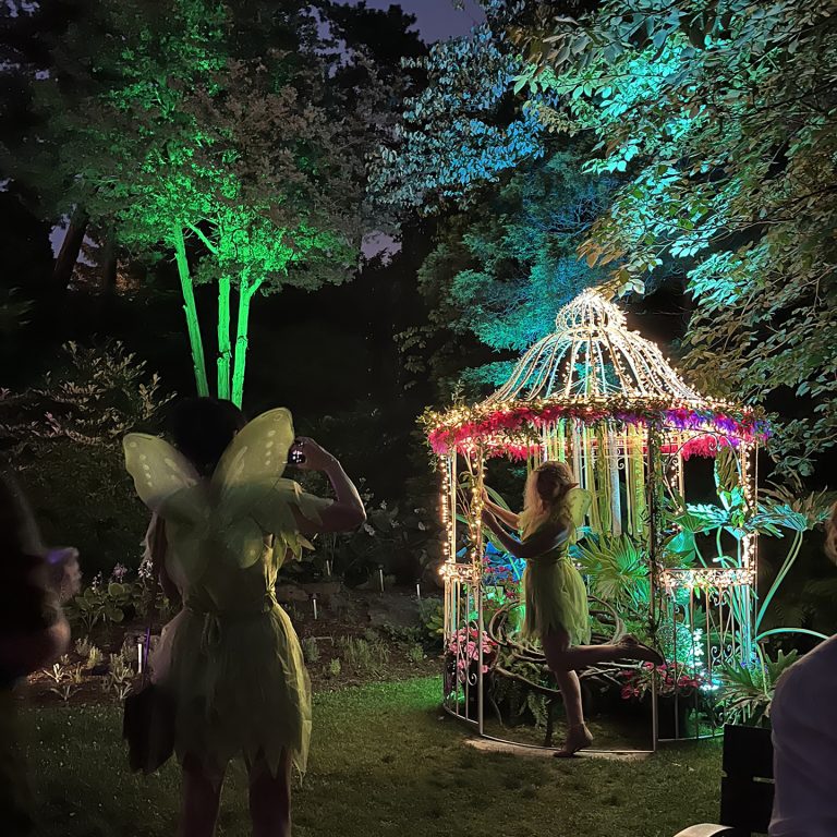 woman dressed as tinkerbell posing with a lit up gazebo in the Rock Garden