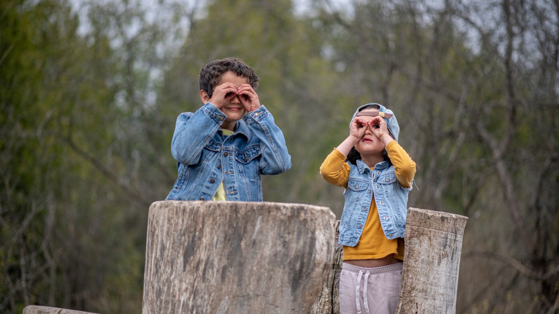 two kids using their hands as binoculars to look at the forest around them