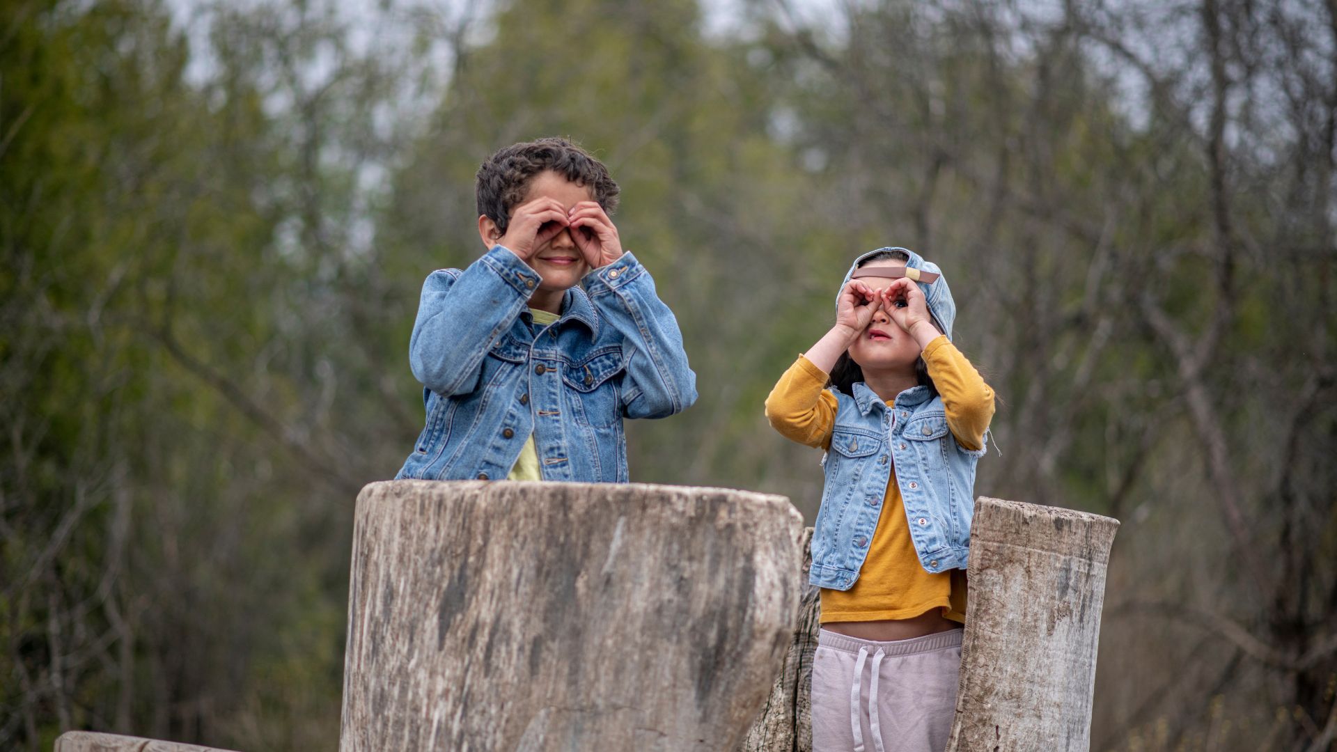 two kids using their hands as binoculars to look at the forest around them